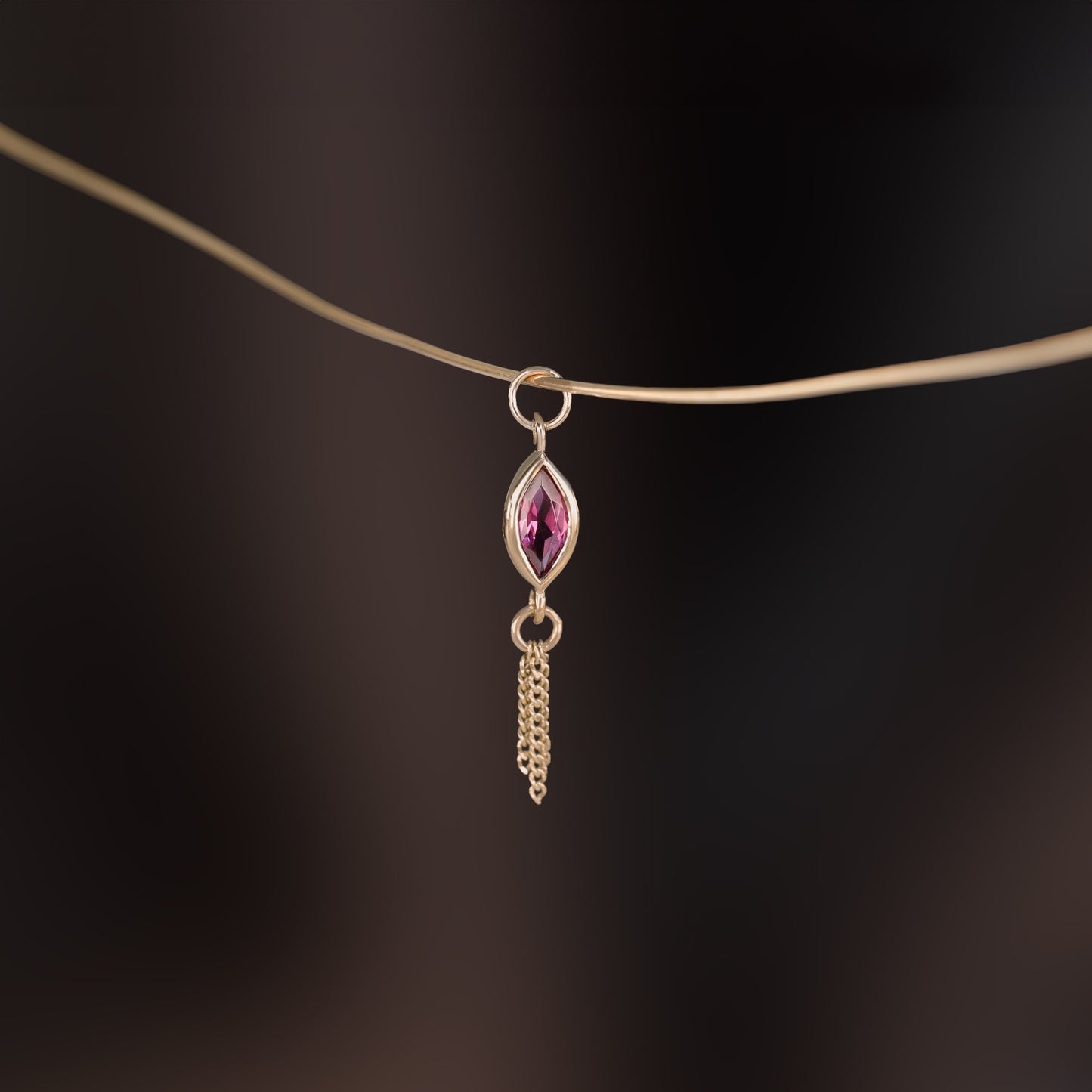 14K gold charm of a marquise-cut Rhodolite Garnet paired with three delicate gold curb chain tassels