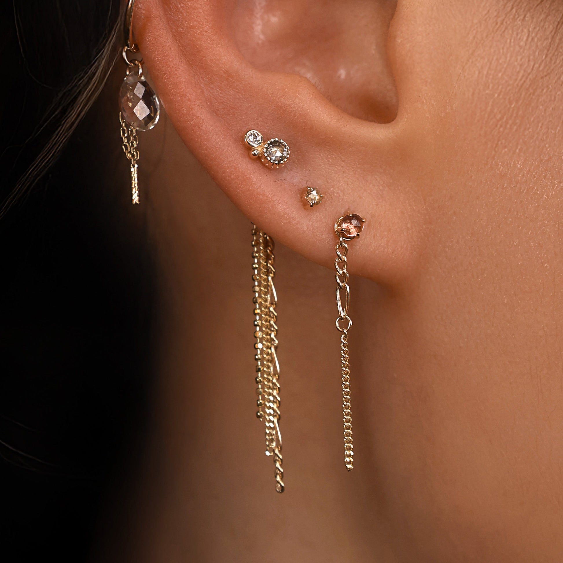 Close-up of an ear with multiple gold earrings against a dark background