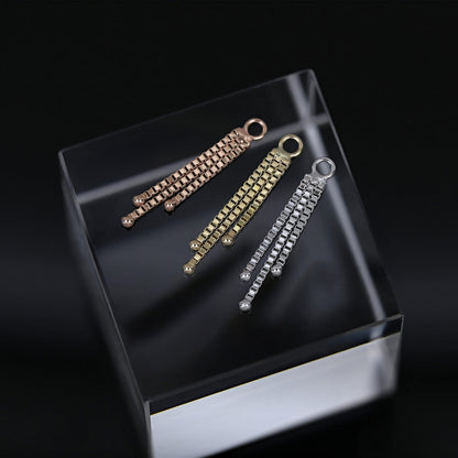 Rose, yellow, and white gold chain charms on a clear cube, set against a dark background