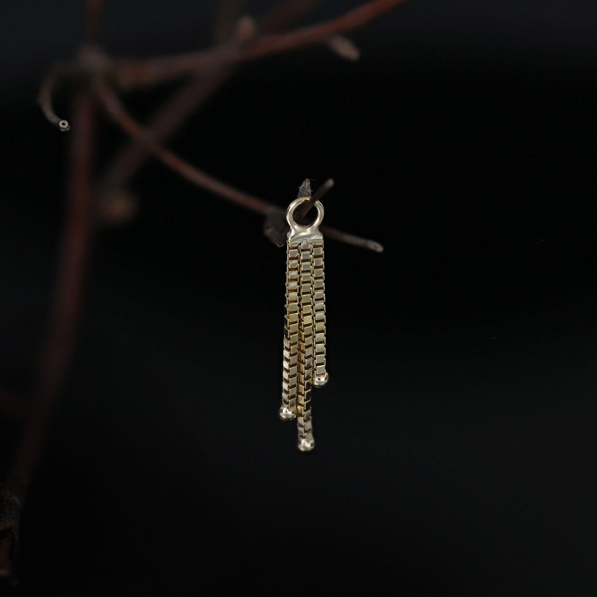 Gold chain charm hanging on a branch with black background